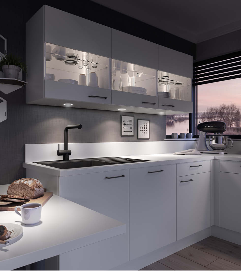 Moderne, helle Küche mit weißen Fronten und klarer Linienführung, beleuchtet durch warmes LED-Licht unter den Hängeschränken. Auf der Arbeitsplatte stehen eine Küchenmaschine, Brot und eine Tasse Kaffee – alles in einer gemütlichen Abendstimmung mit Blick durchs Fenster.