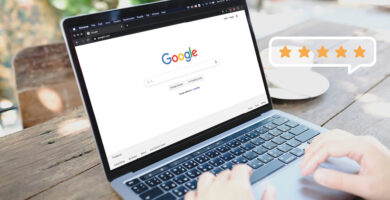 Laptop mit geöffneter Google-Startseite auf einem Holztisch, daneben eine Tasse Kaffee – daneben eine eingeblendete 5-Sterne-Bewertung.