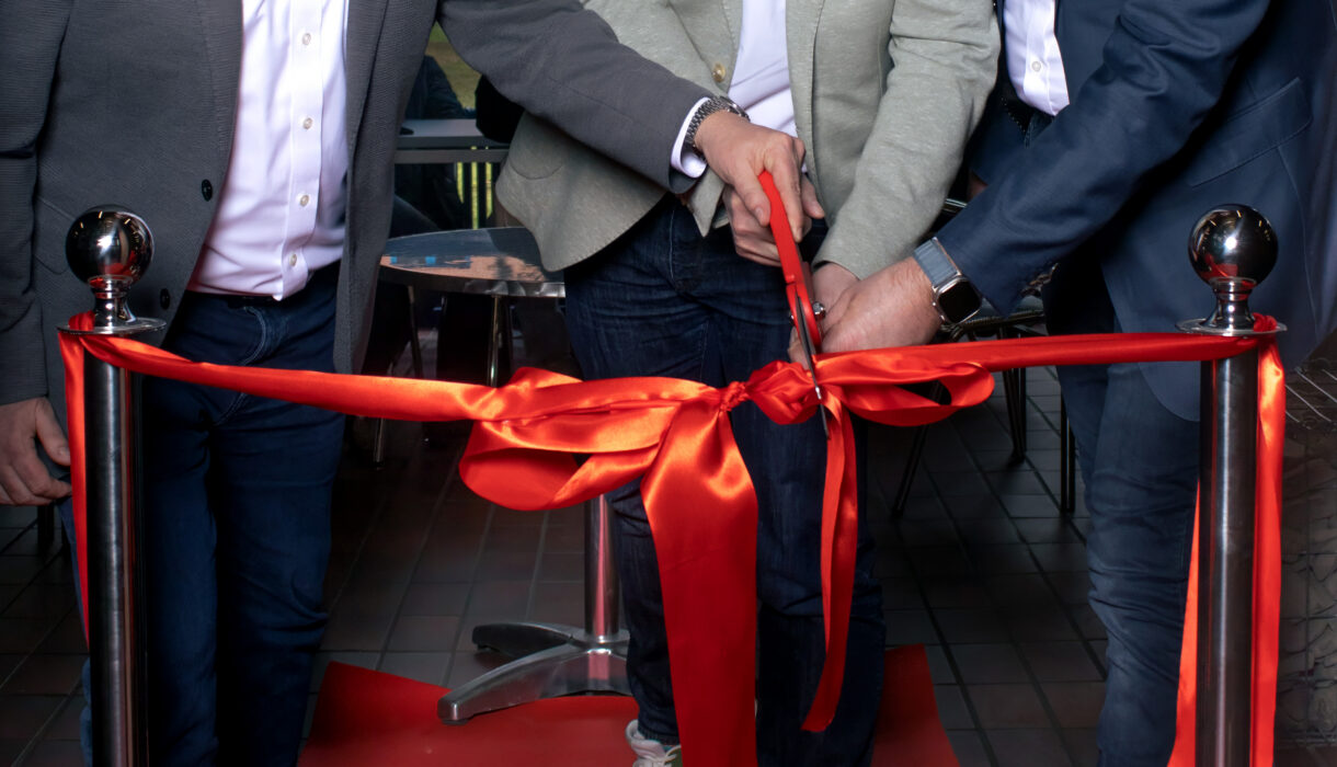 Rote Schleife wird von den Geschäftsführern mit einer Schere bei der Neueröffnung des MöFa Schulungsraumes durchgeschnitten