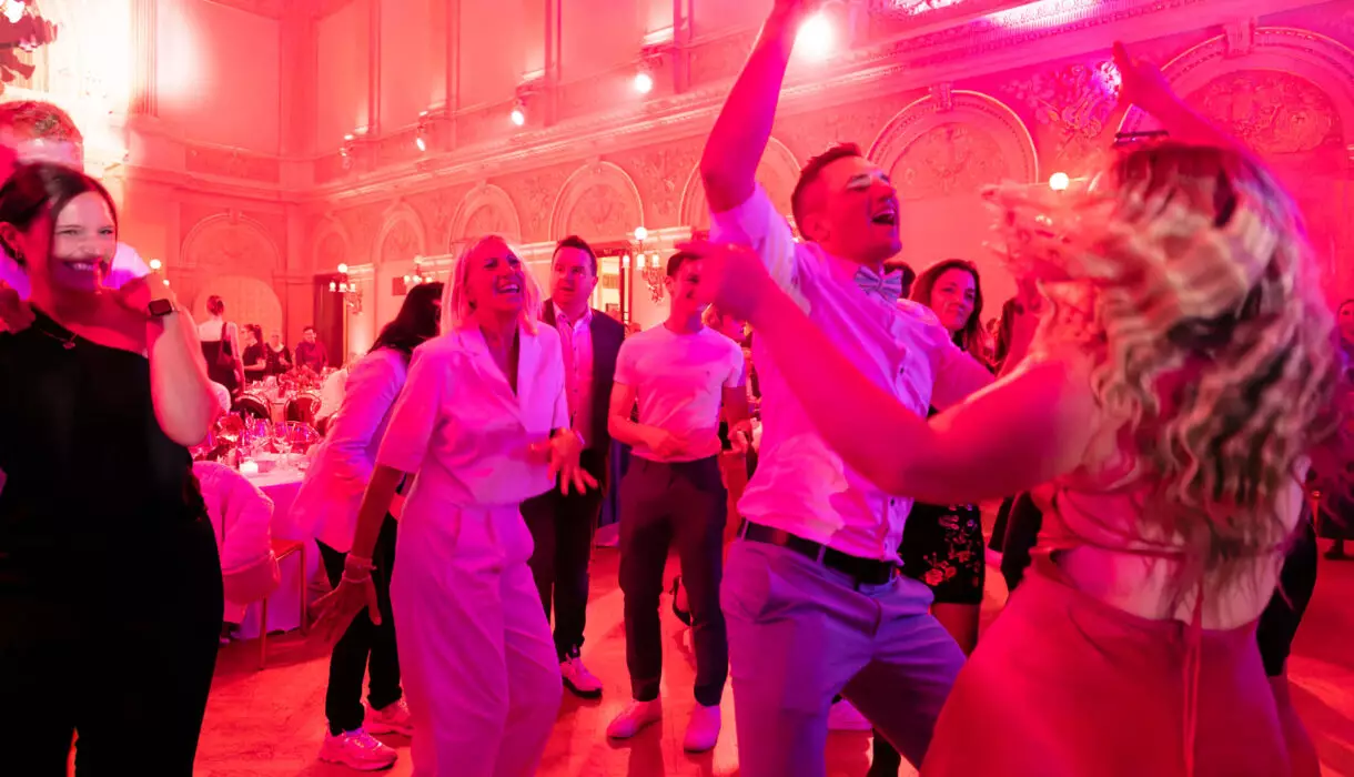 Menschen tanzen freudig in einem großen, pompösen Festsaal.