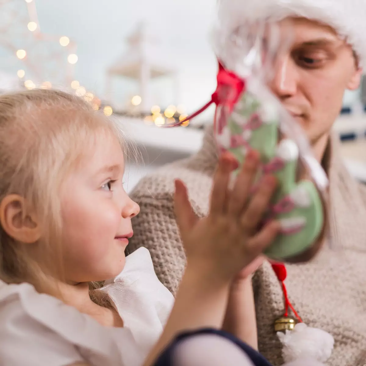 Kleines Mädchen freut sich über ein liebevoll verpacktes Weihnachtsgeschenk und blickt lächelnd auf ihren Vater