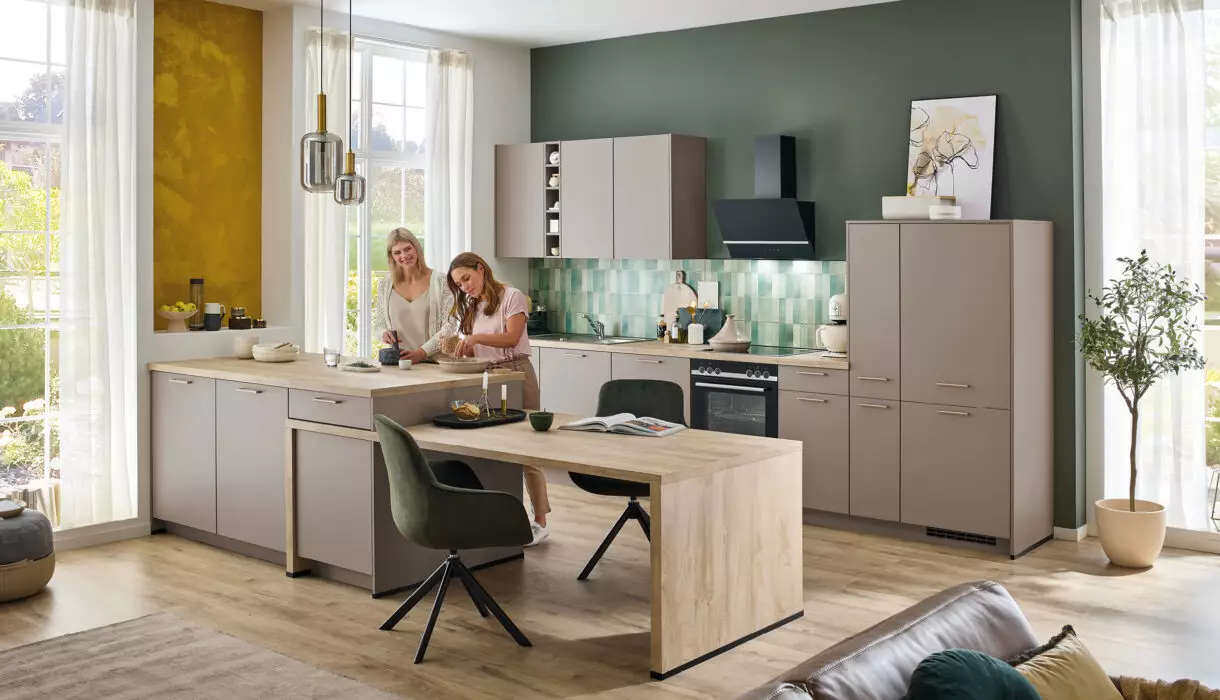 Zwei Frauen bereiten gemeinsam Essen in heller moderner Küche mit Holzelementen und grüner Wandgestaltung zu – stilvolles deutsches Küchendesign mit Wohlfühlatmosphäre.